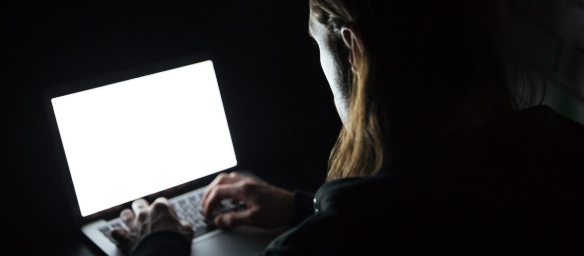 Image of young man using laptop computer at home indoors at night. Looking at laptop display.